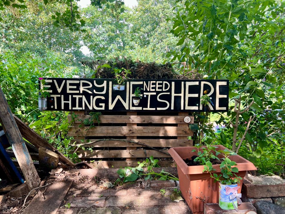 A hand painted sign that reads “everything we need is here” fixed to the compost bin of Folkestone’s Community Sculpture Garden - Community Art Kent 