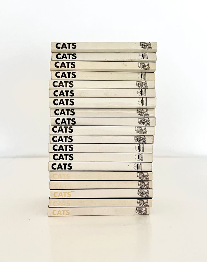 Pile of books; the same small white book (some different editions) with the title “CATS” in black bold font on the spine 