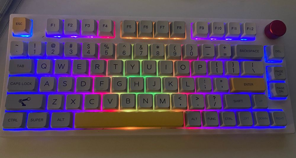 A dark picture with a short 80% mechanical keyboard. There's rainbow lights backlighting the grey keys.