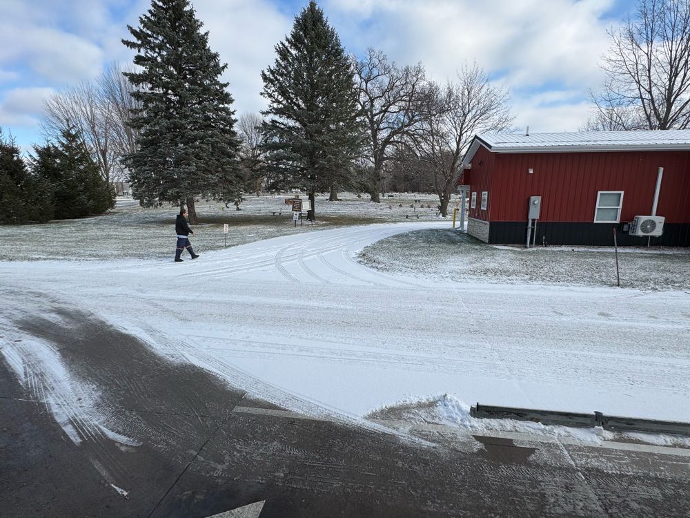 The view from our drive-thru window: a barn house looking shed and a snow-covered cemetery across the way with a person walking by.
