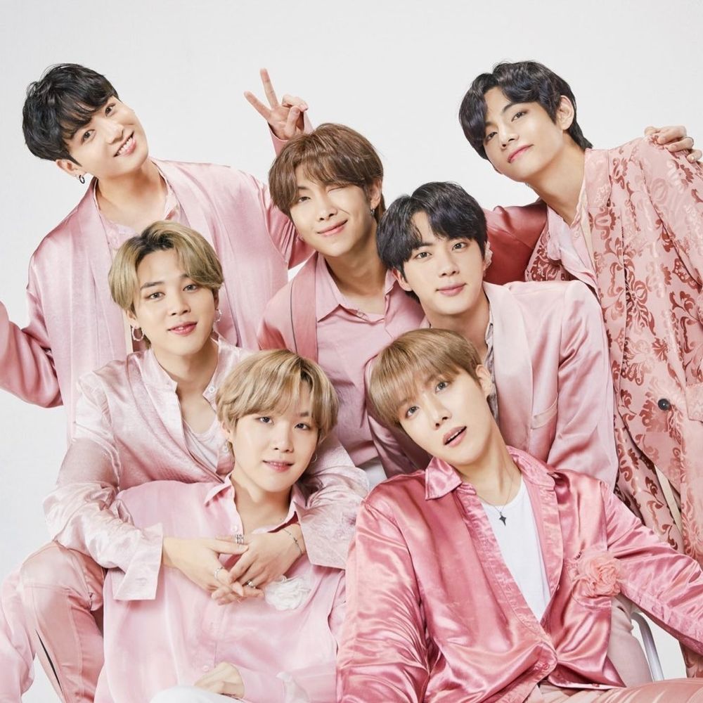 The 7 members of Korean boy band BTS clad in silky satin baby pink outfits, posing with small smiles