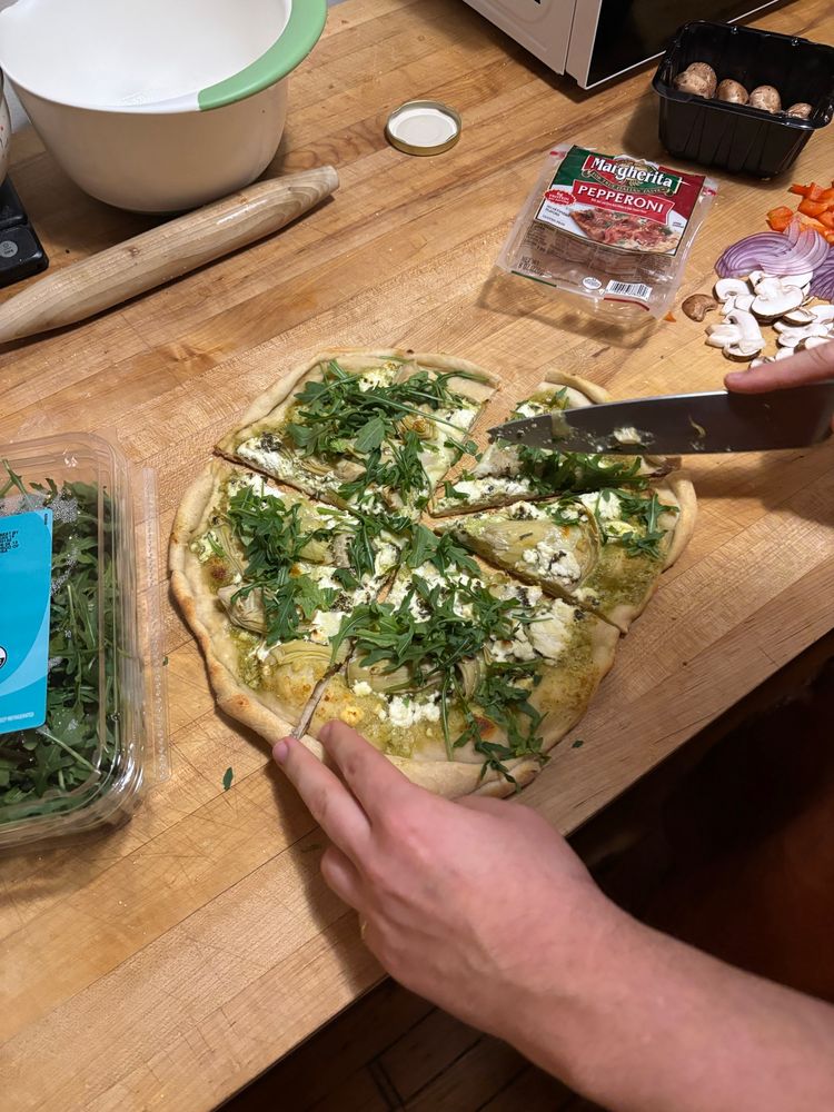 Finished pizza with arugula, goat cheese, artichoke hearts and pesto 