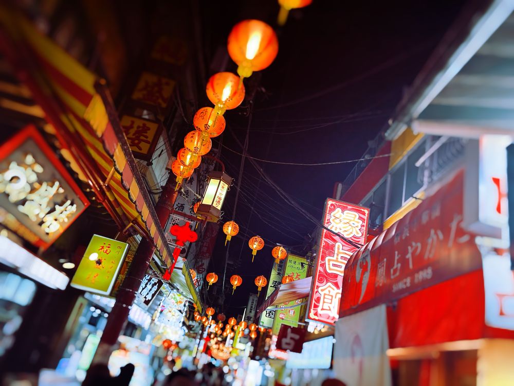 ランタン型の灯りが街路に吊るされた小道の写真。店先の看板も明るくにぎやかな雰囲気
