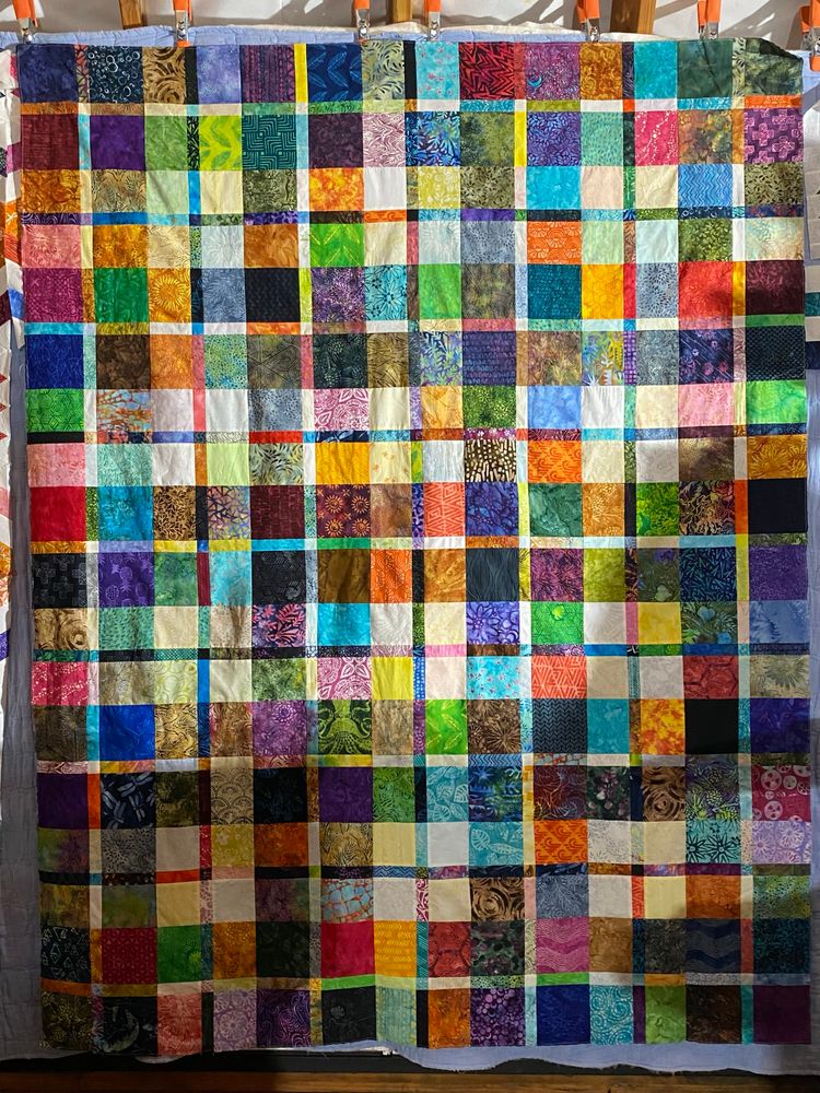 A scrappy plaid quilt hangs on a wall moments after last seem was sewn. 