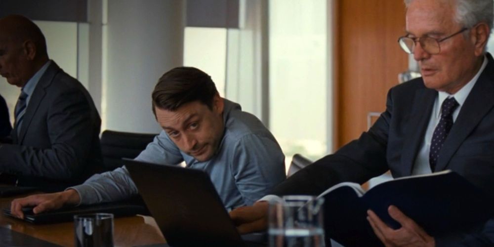 Roman Roy in succession cringing behind a laptop at an executive board meeting 