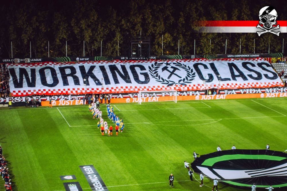 Tifo de la afición del rayo. Es una pancarta blanca, con los bordes rojos que dice en negro: WORKING CLASS. En el centro, también en negro, hay un símbolo de dos martillos cruzados enmarcados entre hojas de laurel