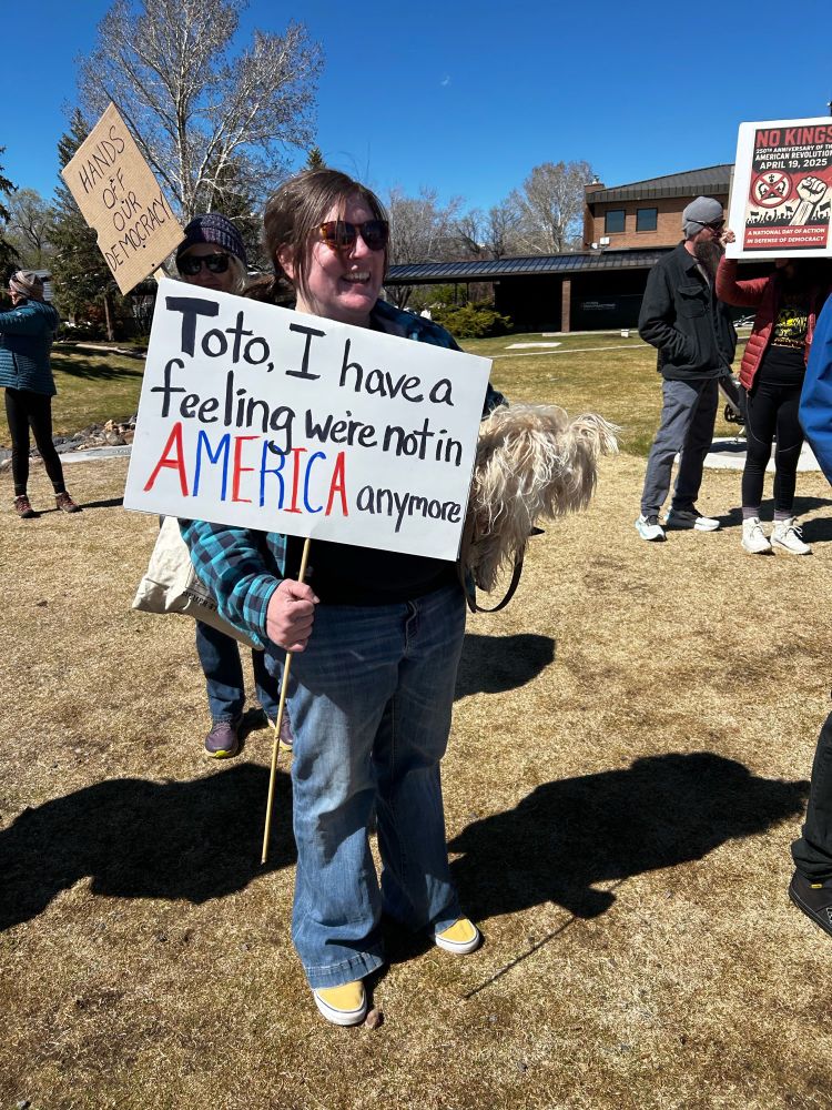 Person holding a dog carries a sign that says “Toto, I have a feeling we’re not in America anymore.”