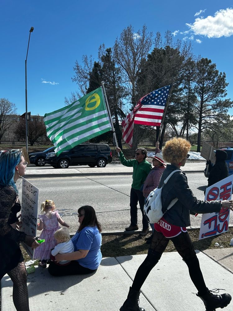 People flying the US flag and ecology flag while a young person walks by with a Hands Off sign.