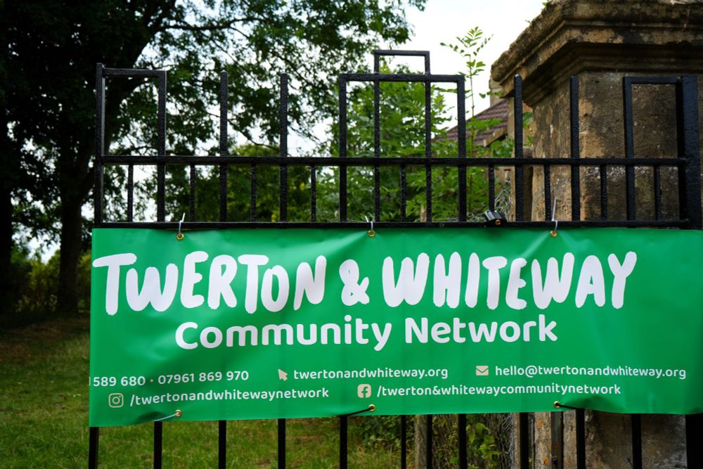 A green vinyl banner attached to railings with the words "Twerton and Whiteway Community Network" in green