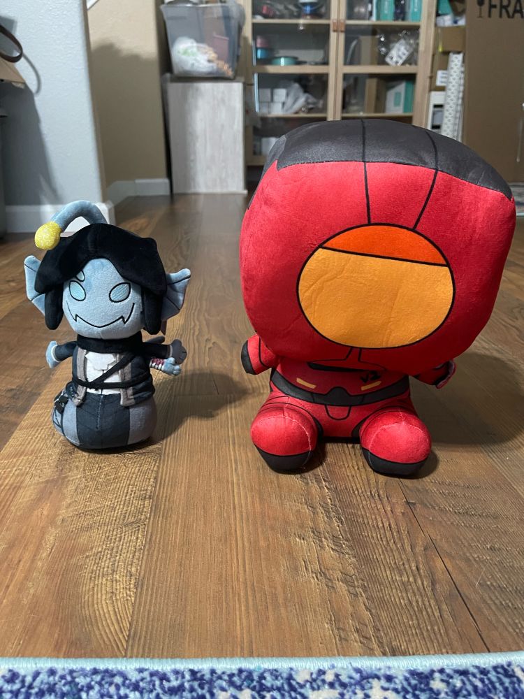 sebastian solace (roblox pressure) plushie and v2 (ultrakill) plushie sitting on the floor next to eachother and staring at the viewer