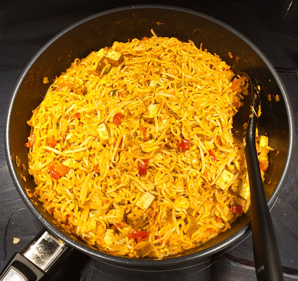 Photo of food in a pan on a stove. Red coconut curry, noodles, bean sprouts, tofu, bell pepper.