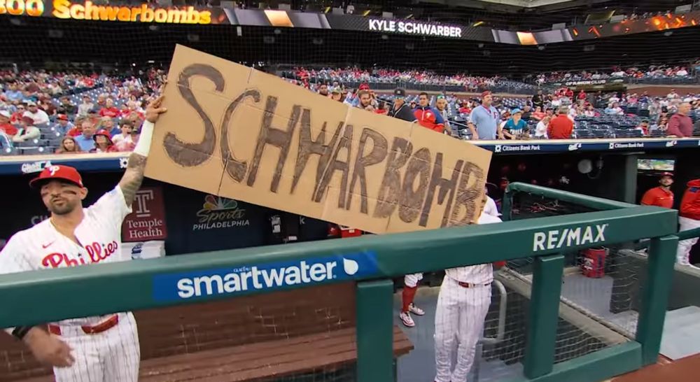 Two Phillies players holding cardboard sign that says Schwarbomb