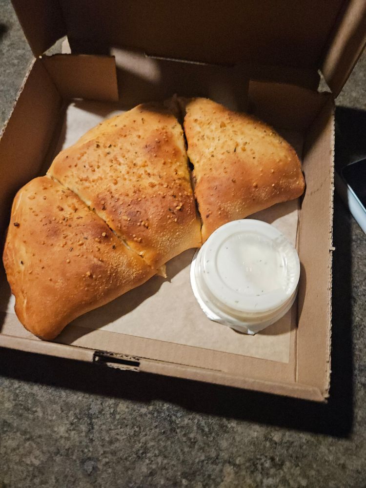 semi-circular bread thing cut into pie slice thirds, like the yeasty Italian version of a quesadilla, in a cardboard takeout box and with an unopened ranch dipping cup in the empty space.