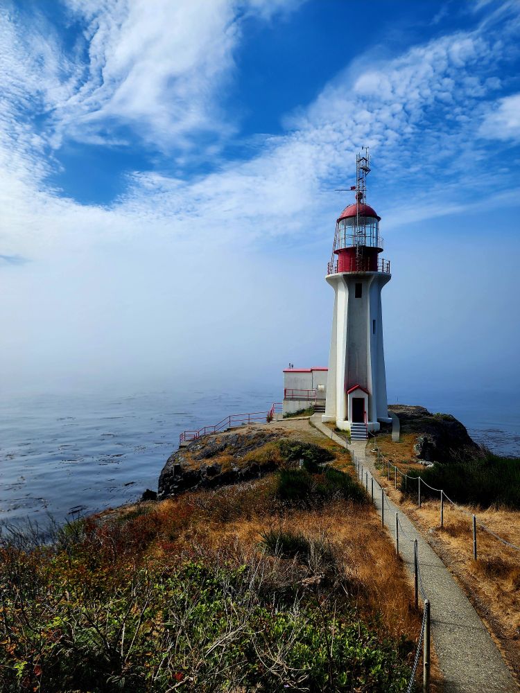 A lighthouse against a blue sky with clouds. 