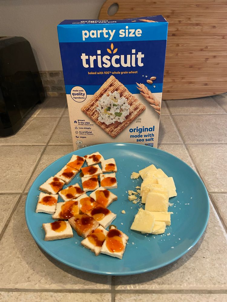 sliced baked tofu covered in 3 hot sauces and sliced coastal cheddar on a blue plate. party size triscuit wants to be topped by them.