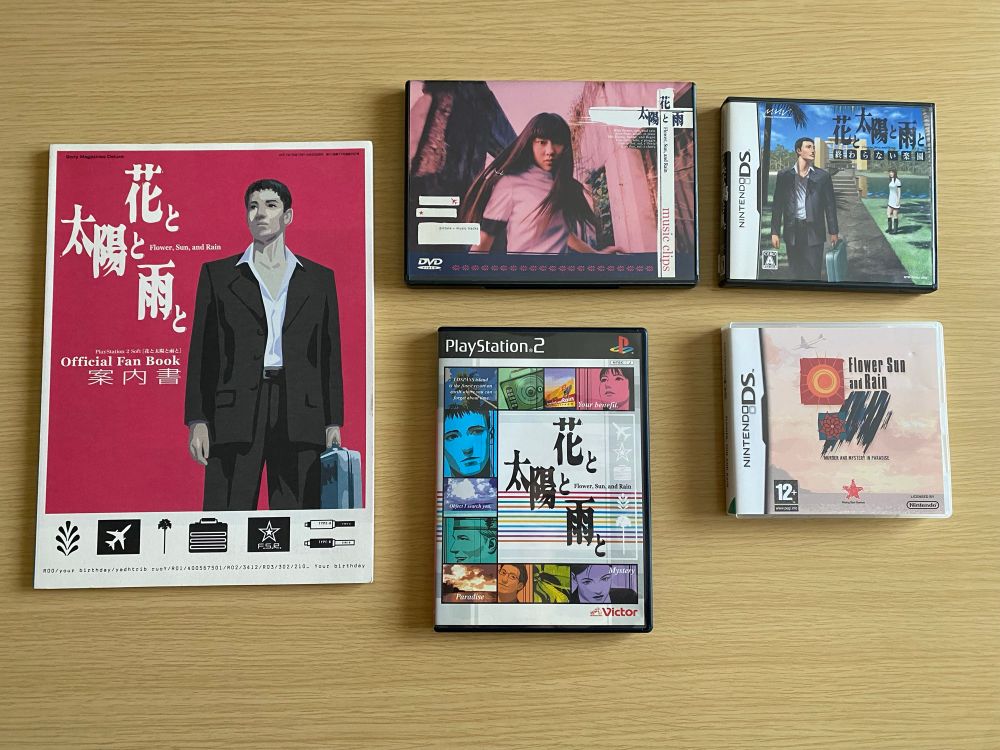 Some Flower, Sun, and Rain nonsense laid out on a table, including the original Japanese PS2 version, the European and Japanese DS versions, the Japanese Official Fan Book and Japanese Music Clips DVD.