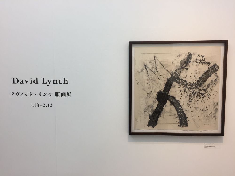 The front wall of the exhibition (デヴィッド・リンチ版画展). There’s an artwork of a smudgy kind of stick figure with wings, maybe, and a twisty possibly-head. In the top left, it says “bug angel weeping”