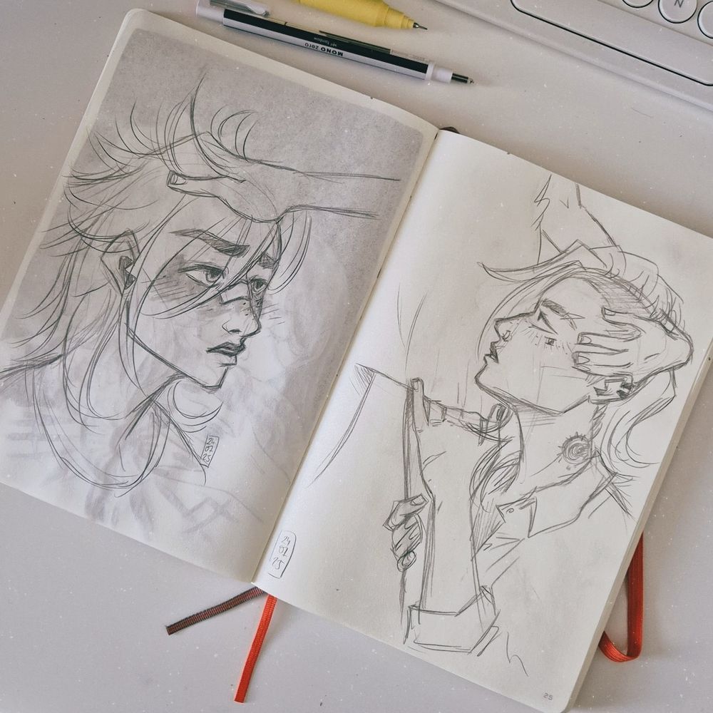 Photo of a sketchbook spread open on a desk, showing two pencil sketches of Vi from Arcane. The one on the left shows a portrait of Vi at a three quarters view. She's blushing and looking up. Caitlyn's hand is laying on Vi's head and ruffles her hair. On the right Vi is seen from her side profile, clinging to Caitlyn's hip and looking up at her. Caitlyn is holding her head, while Vi slips her hand under the hem of Cait's body tight mini skirt. Vi is wearing a loose shirt that opens at the collar.