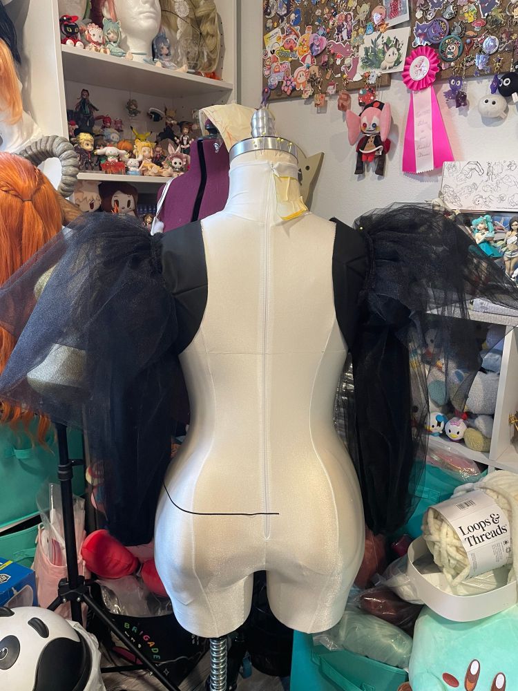 A mannequin with black sleeves and black tulle pinned to it in a messy sewing room