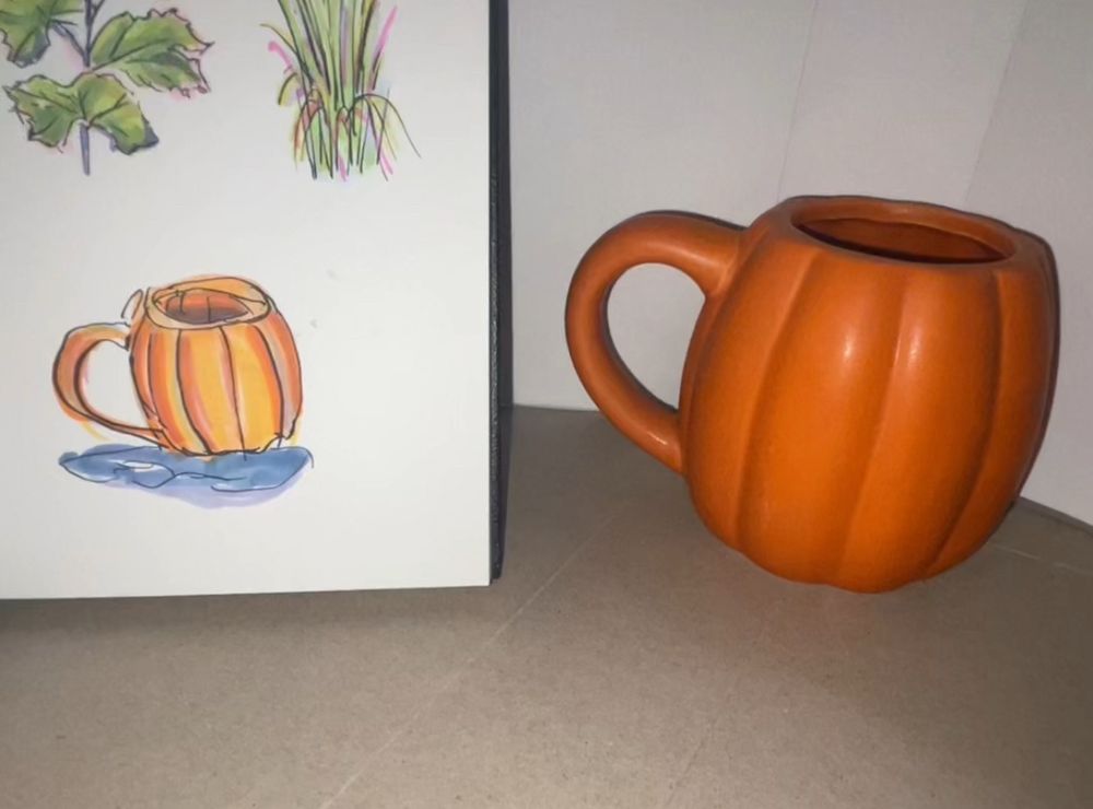 On the right side, we see a orange pumpkin-shaped mug. To the left of that is a drawing of that mug in a sketchbook. above the mug, we see sketches of leaves and some grass which are cut off by the top of the photo. 