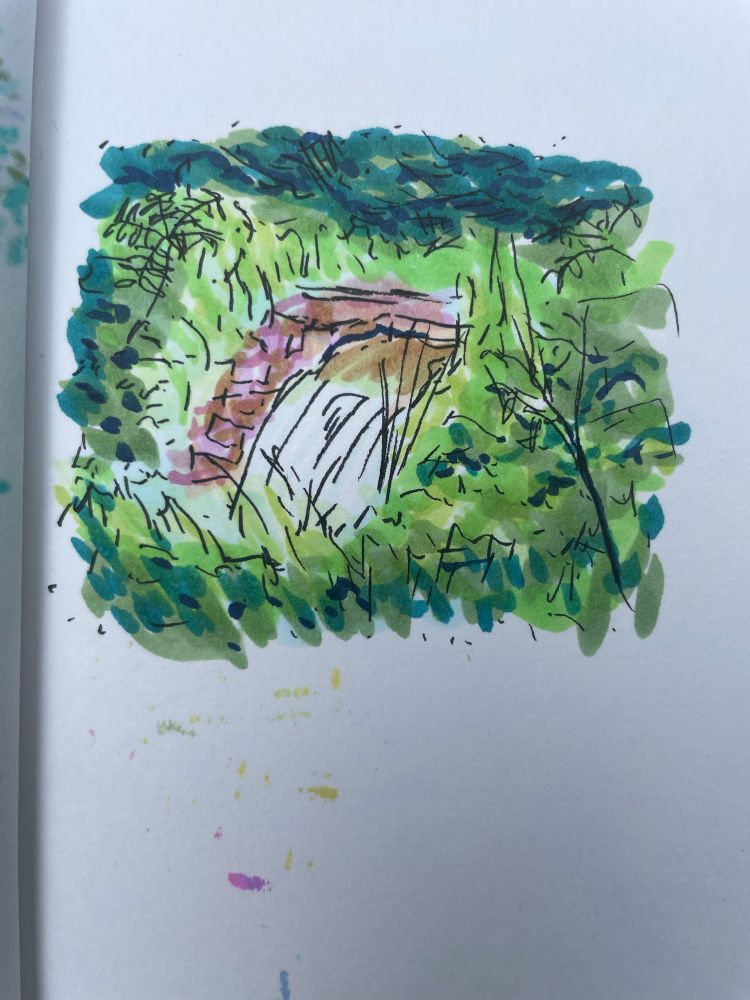 We see a close up of the marker sketch. Things are colorful and bright. The waterfall falls across a brick wall, and is surrounded by green growth. 