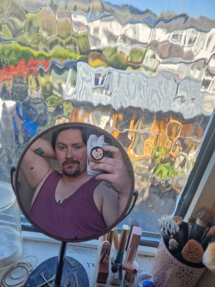 An image of Bel cropped in a small makeup mirror beside a makeup brush holder.