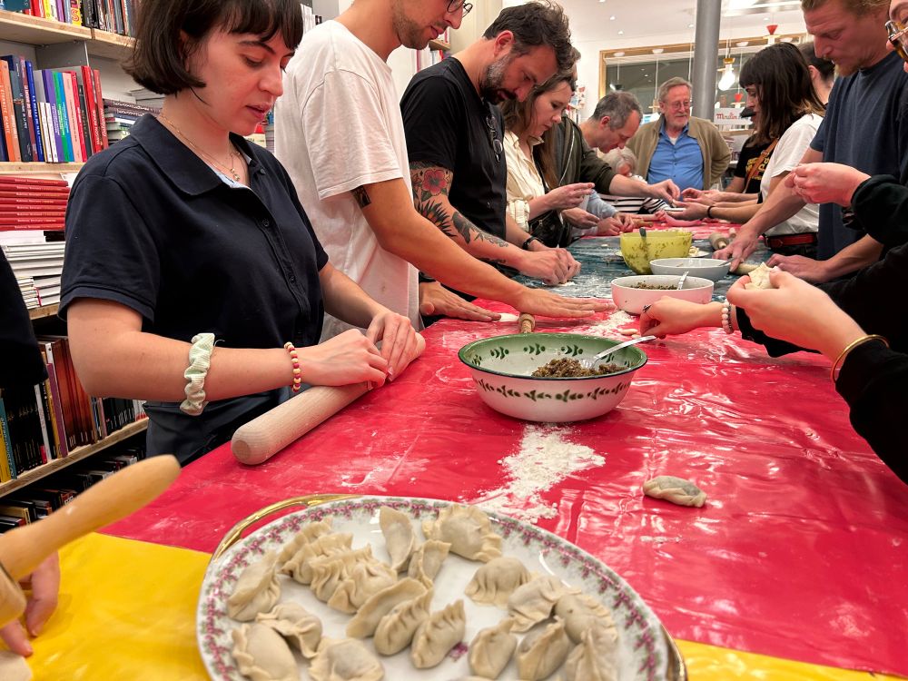 Pour le lancement du Raviolivre, nous avons mis les mains à la pâte ! Ravioles préparés collectivement. De chaque côté de la table des gens préparent des ravioles, ceux qui sont prêts sont sur une assiette au premier plan.  