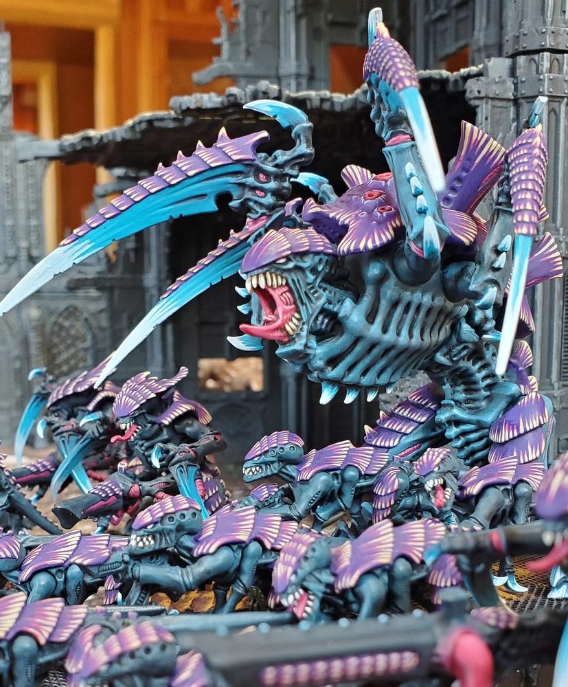 A fierce horde of ravenous creatures fill the ruins of a destroyed city. The creatures' dark flesh and patterned back armor is contrasted by their ice-cold talons and pink hungering maws