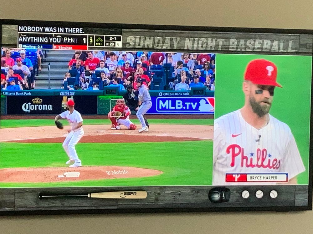 Screen shot of Christopher Sanchez throwing a pitch while Bryce Harper is being interviewed by the ESPN dingbats