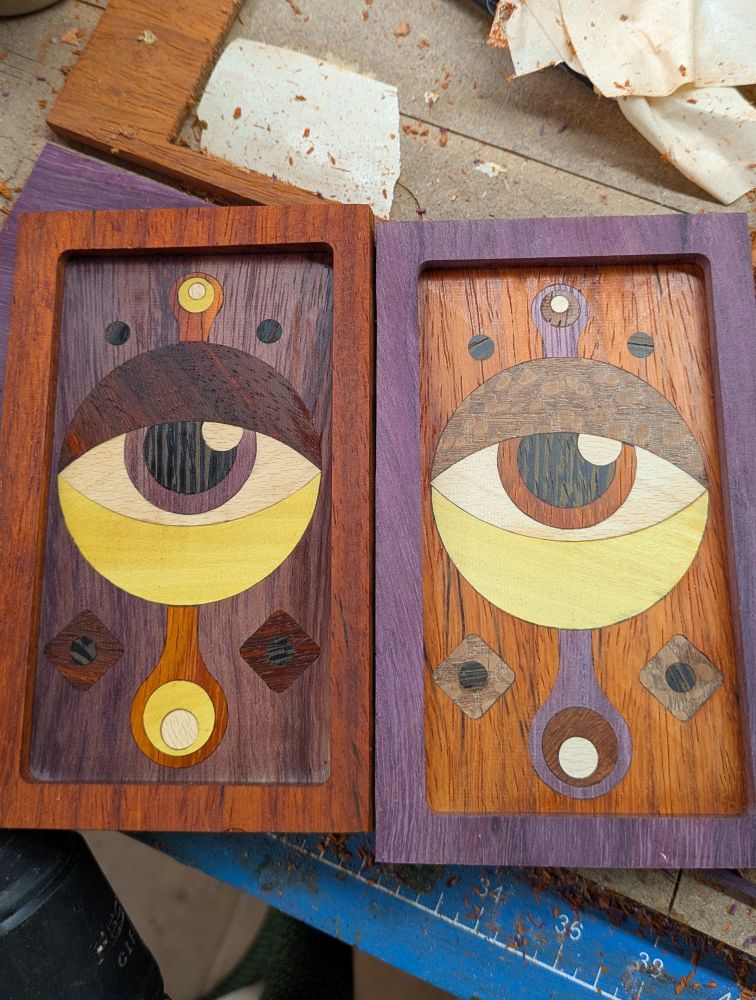Two framed pieces of wood in different colors with abstract wood inlay of eyes I'm several different colored woods sort of side by side