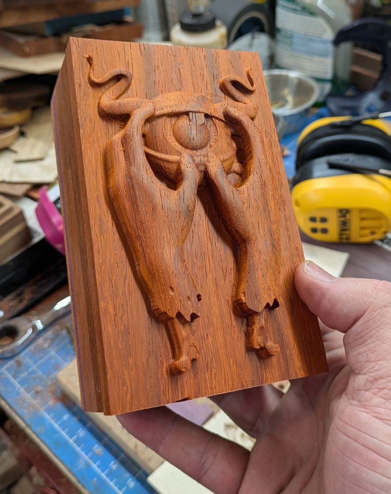A wooden box with carved lid featuring two severed hands holding an eye with horns carved deep into the lid 