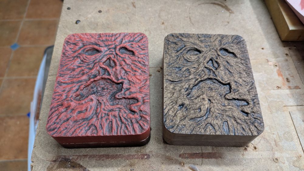 Two boxes carved with the human face book cover from the evil dead, one painted red and dark tones and the other natural walnut with some darkening. 