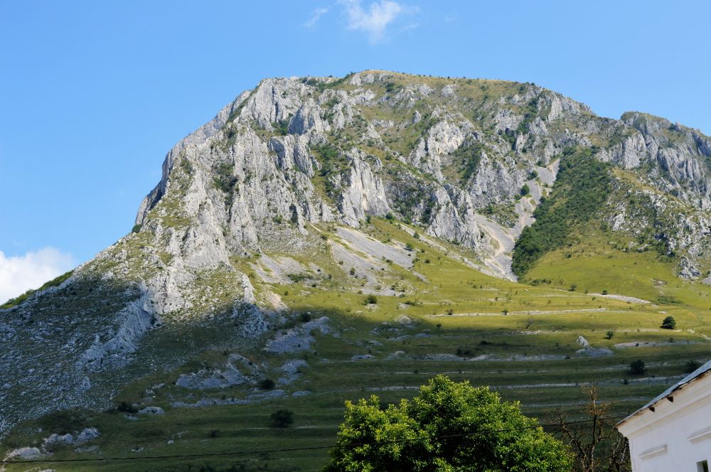 Blick auf einen gewaltigen Felsen, der teilweise begrünt ist. Strahlend blauer Himmel