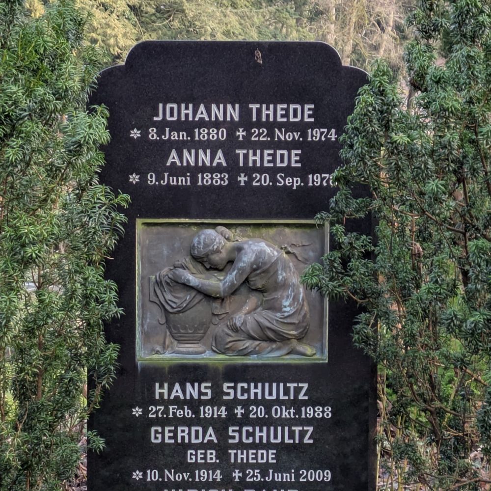 schwarzer Grabstein mit Inschriften und Bronzerelief: eine Frau kniet vor einer Urne
