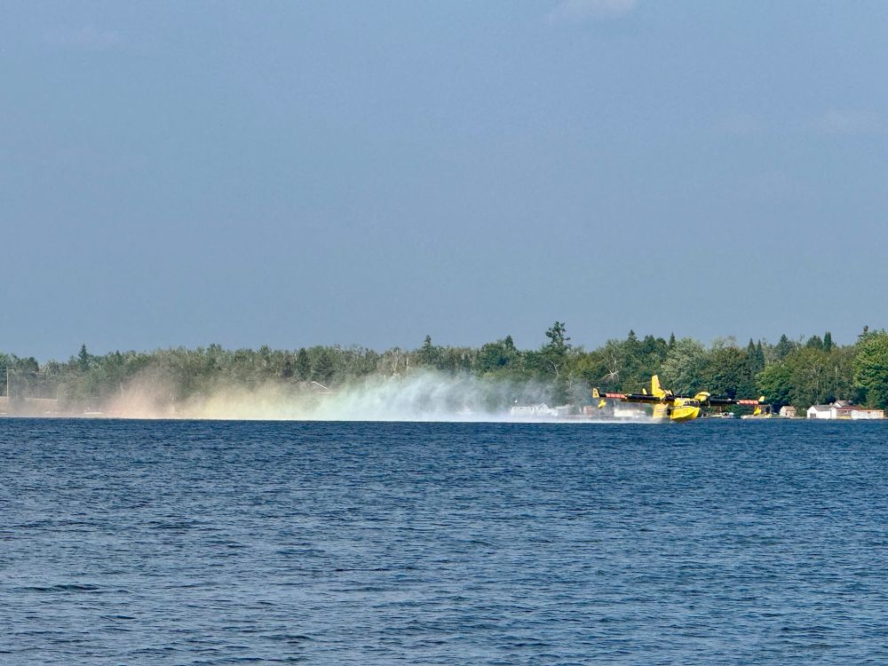 Yellow water bomber picking up lake water surface to put out forest fire. 