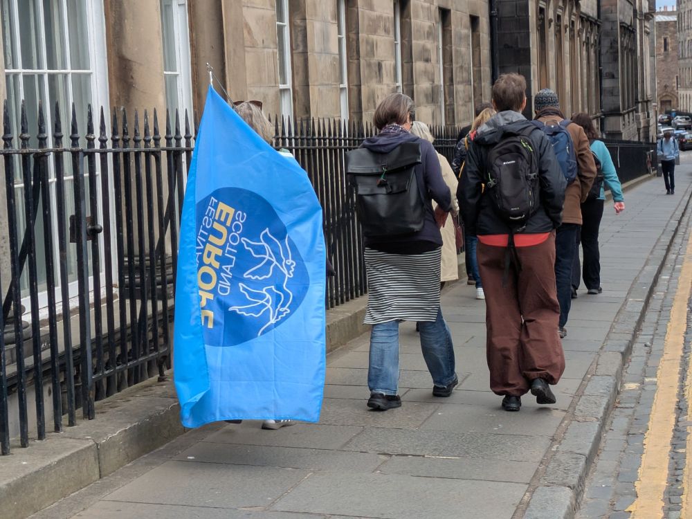 walking on pavements with one walker with a blue Festival of Europe Scotland flag