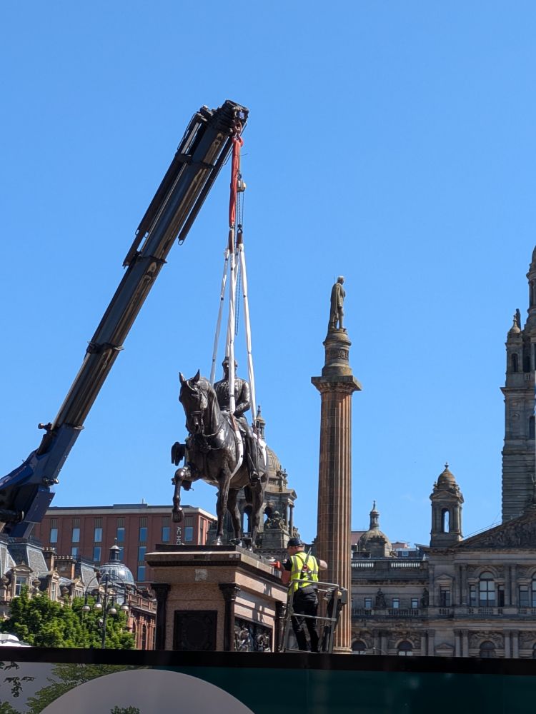 Horse statue being lifted by a crane with straps around the atatue