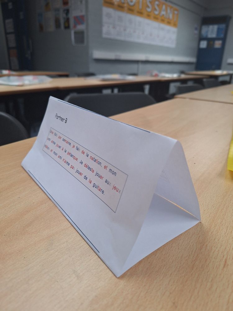 Paper folded to make a triangular prism and standing up on a desk. One side says partner B and a short text in French