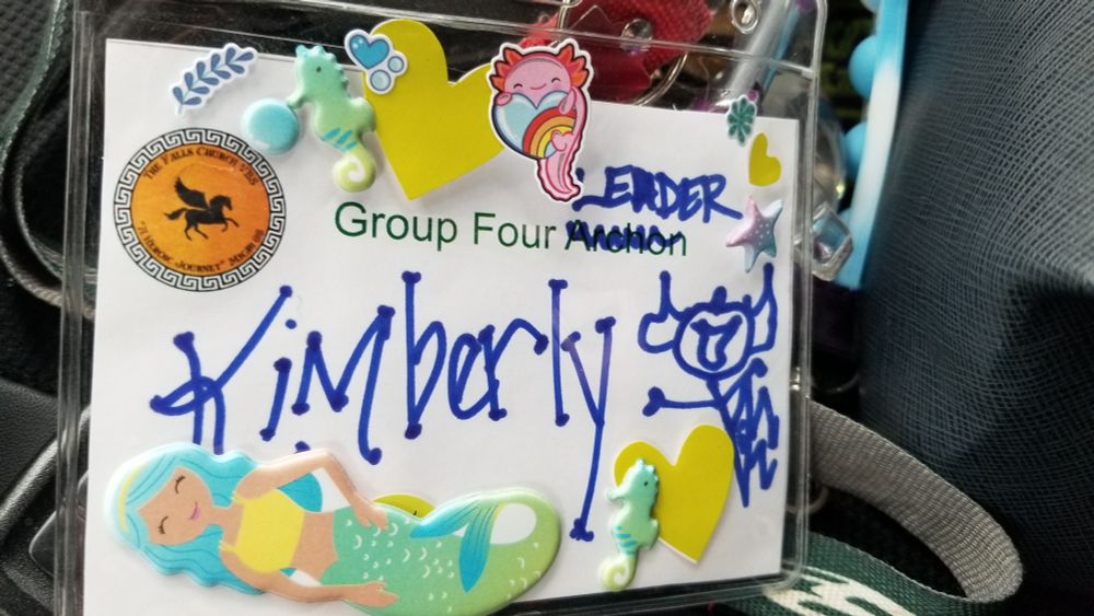 A badge worn by Group Four's Leader at Camp Half Blood covered with stickers from the week's adventure. Stickers include a cute axolotl, seahorses, a mermaid and other such joy-cultivating tokens of a great week.