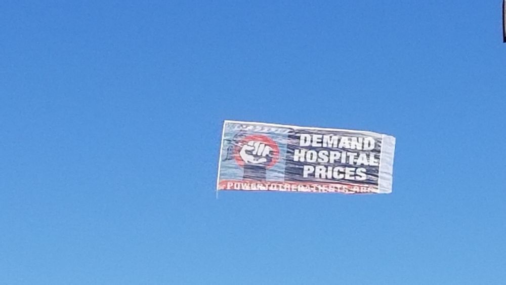 Close up of the banner which reads "DEMAND HOSPITAL PRICES" sponsored by power.... .org (the rest of the domain is illegible)