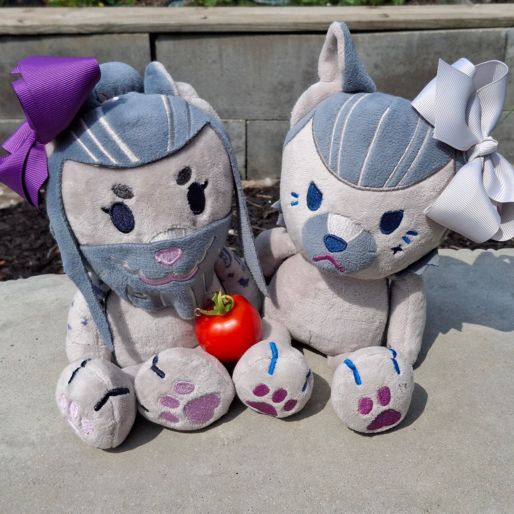 Doggy Izzy and Wolf Ed plushes sitting on a garden bench with a small tomato 
