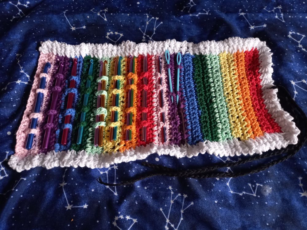 A crocheted rainbow crochet hook roll, opened so you can see the hooks and yarn needles stored inside
