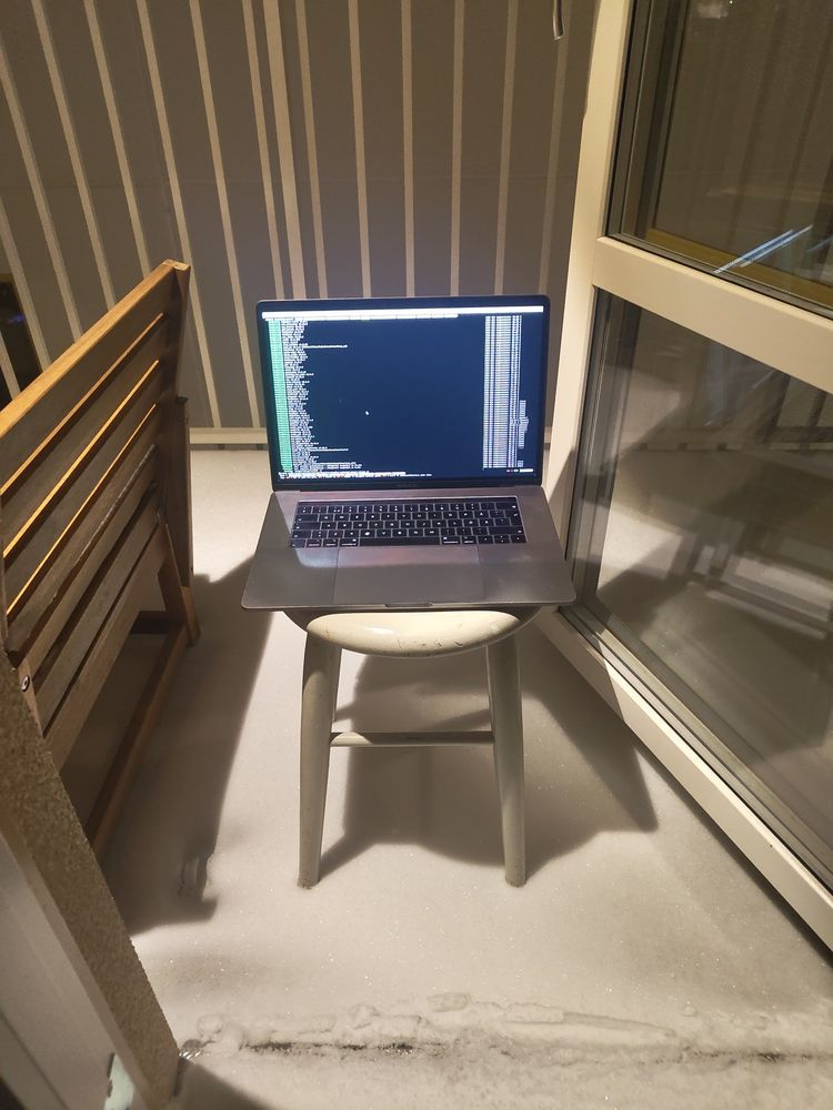 A 2019 MacBook Pro 16" sitting outside on my balcony on a stool in the snow. On the display a terminal running the Nova test262 runner.