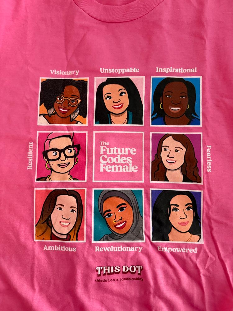 A bright pink T-shirt featuring a grid of illustrated portraits of eight diverse women, each labeled with a positive trait: “Visionary,” “Unstoppable,” “Inspirational,” “Resilient,” “Fearless,” “Ambitious,” “Revolutionary,” and “Empowered.” In the center of the grid is a square that reads “The Future Codes Female.” At the bottom, the shirt is branded with “THIS DOT” and “thisdot.co x jacob ashley.