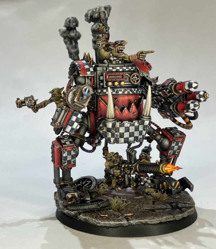 A 40k Killa Kan model that has been modified with longer “legs” to allow an underslung mounted machine gun with a Grot shoota blazing away.  Three other grots are facing other directions either shooting pistols or gesturing vigorously. 