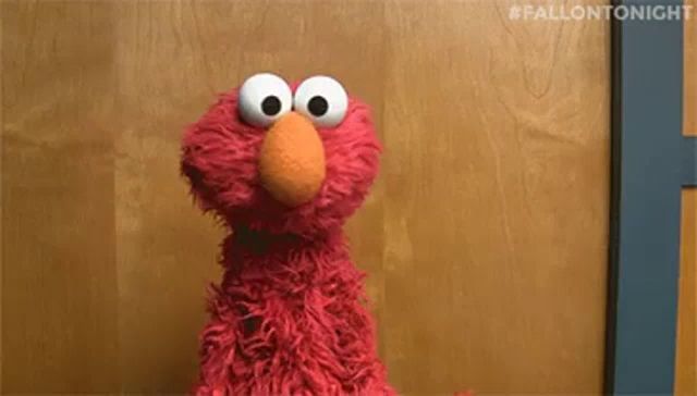 elmo from sesame street is sitting in front of a wooden wall and looking at the camera .