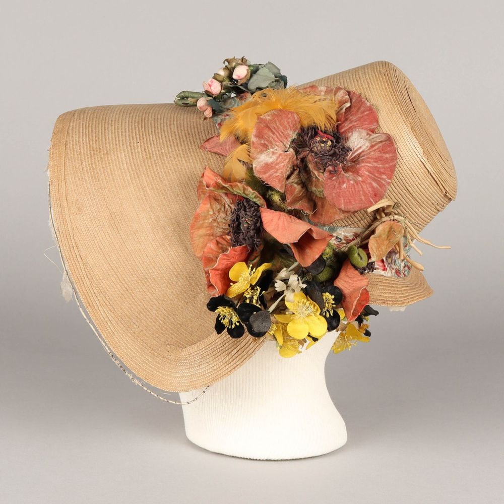 Woman's straw bonnet in simple style with elaborate decorations of feathers, flowers, and figured moire ribbon. Brim is lined with silk; covered wire around edge.