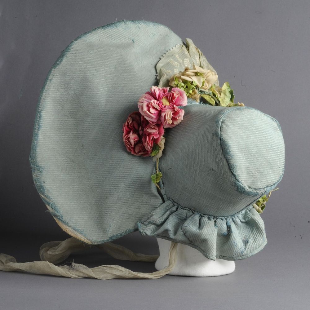 Bonnet covered with blue ribbed silk fabric gauze bow on front brim - a wreath of flowers around the base of the crown - white gauze ties.