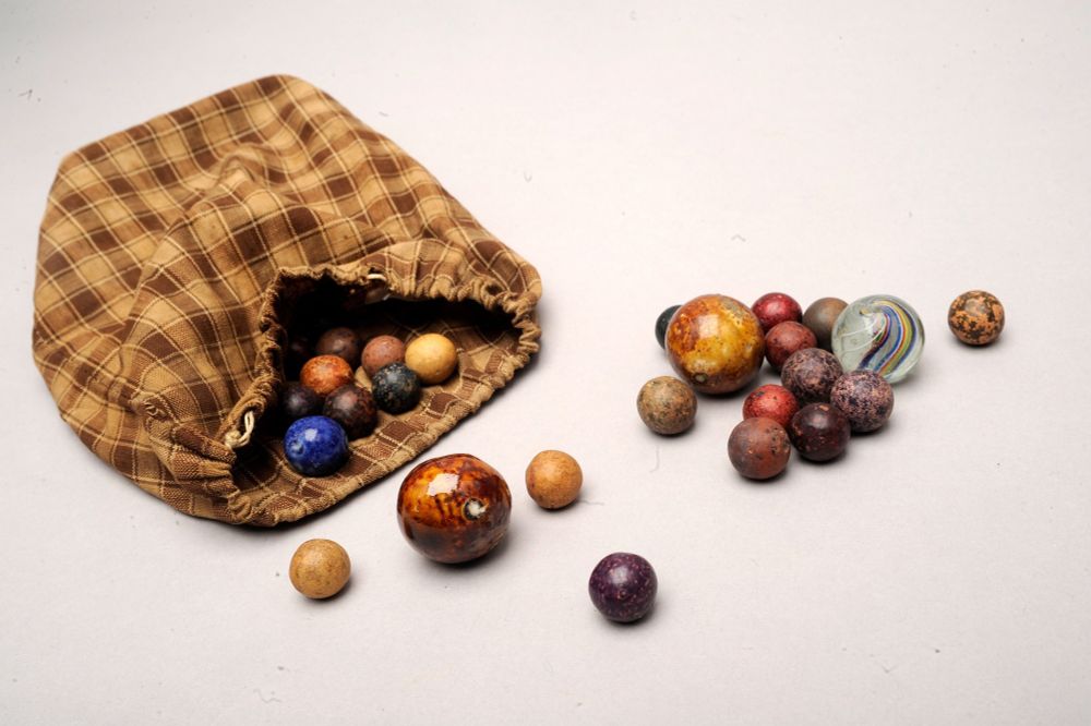 A small plaid fabric pouch and assortment of colorful marbles in small and large sizes