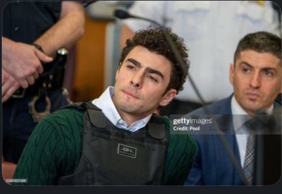 Luigi looking incredulous in a bullet proof vest word over and over an incredible chunky knit sweater in a dark green. 